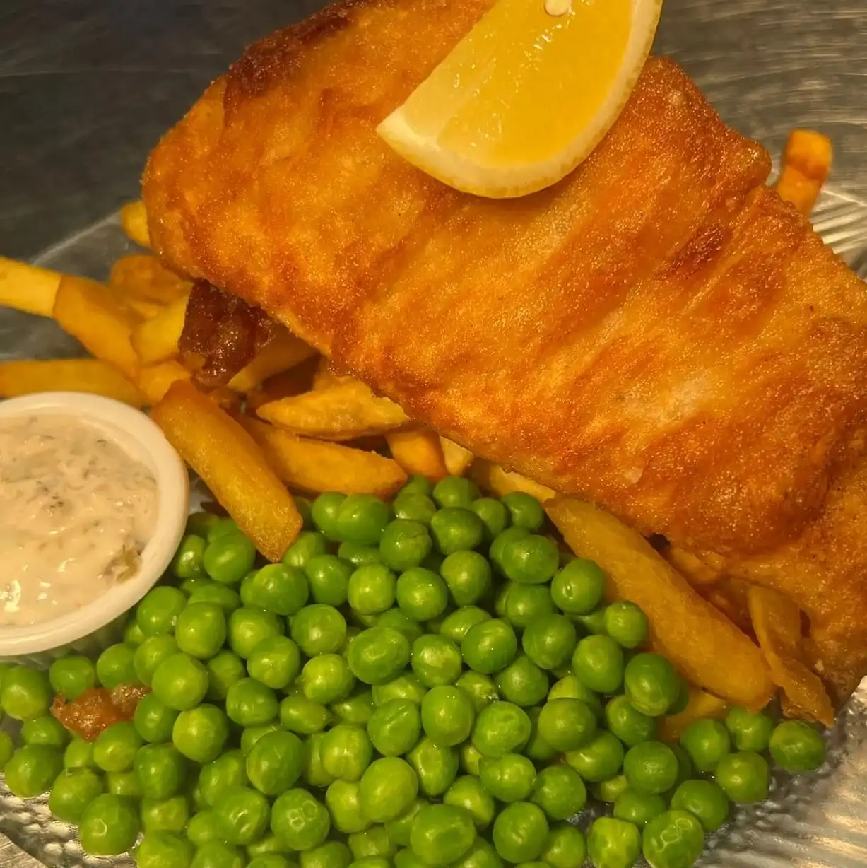 A plate of fish, chips, peas and a lemon wedge.