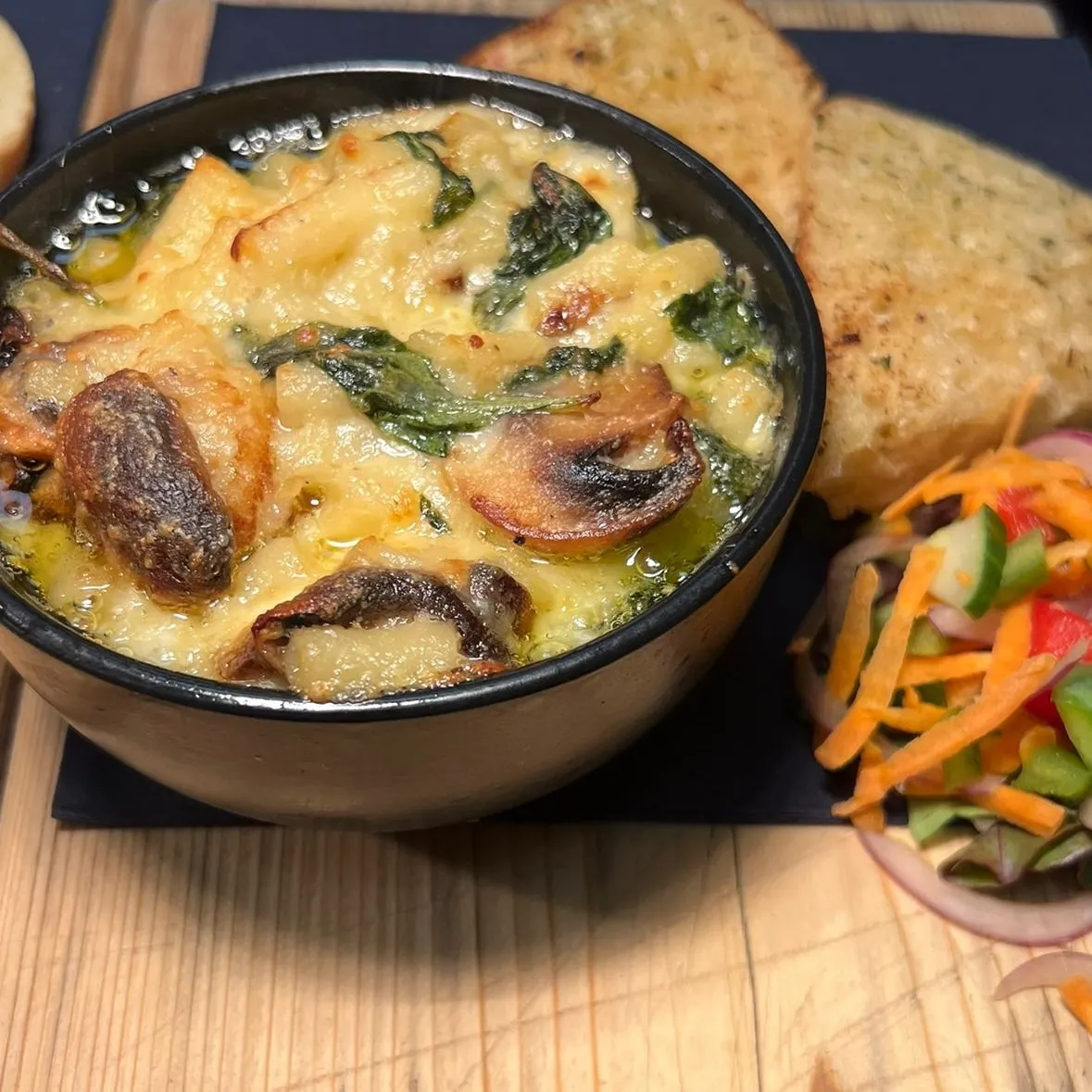 A bowl of food with side salad and garlic bread.