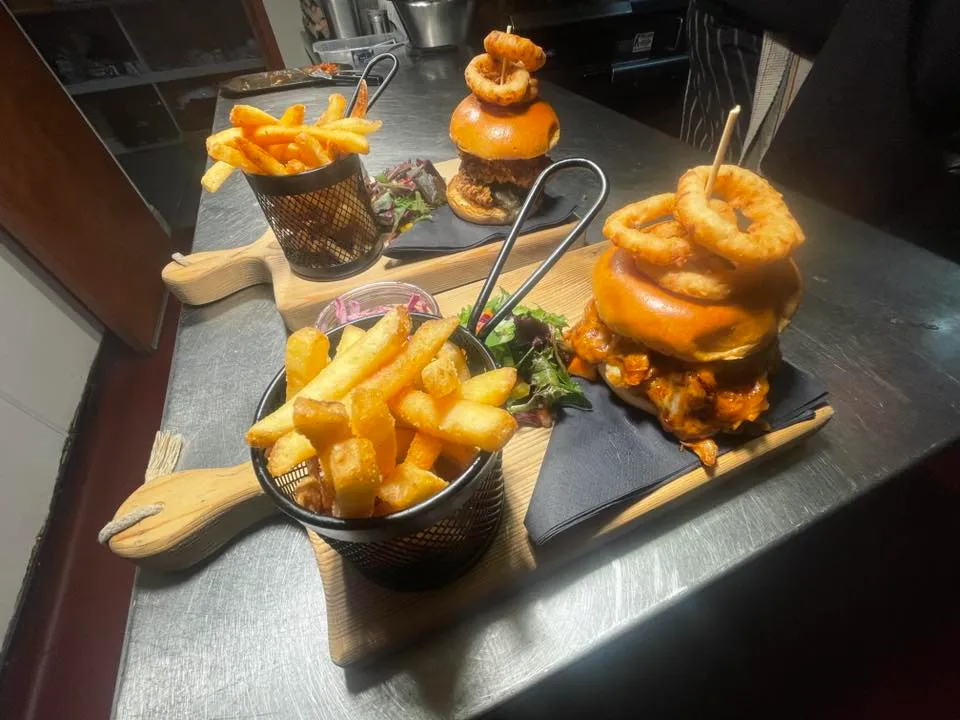 A table topped with plates of burgers, onion rings and chips.