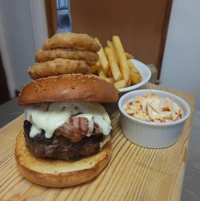 A cheeseburger and chips, with coleslaw and onion rings.