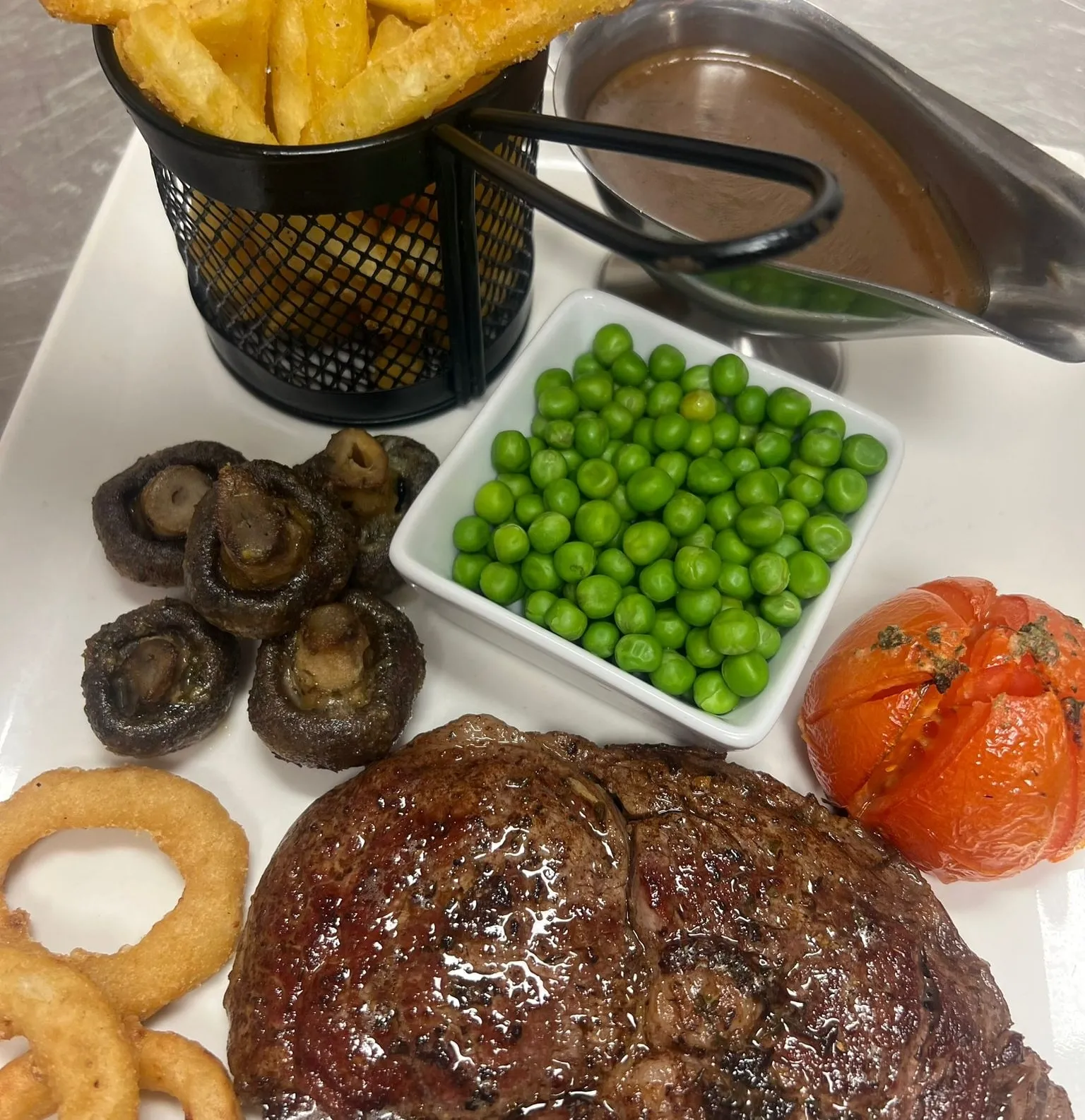 A plate with steak, onion rings, vegetables and gravy.