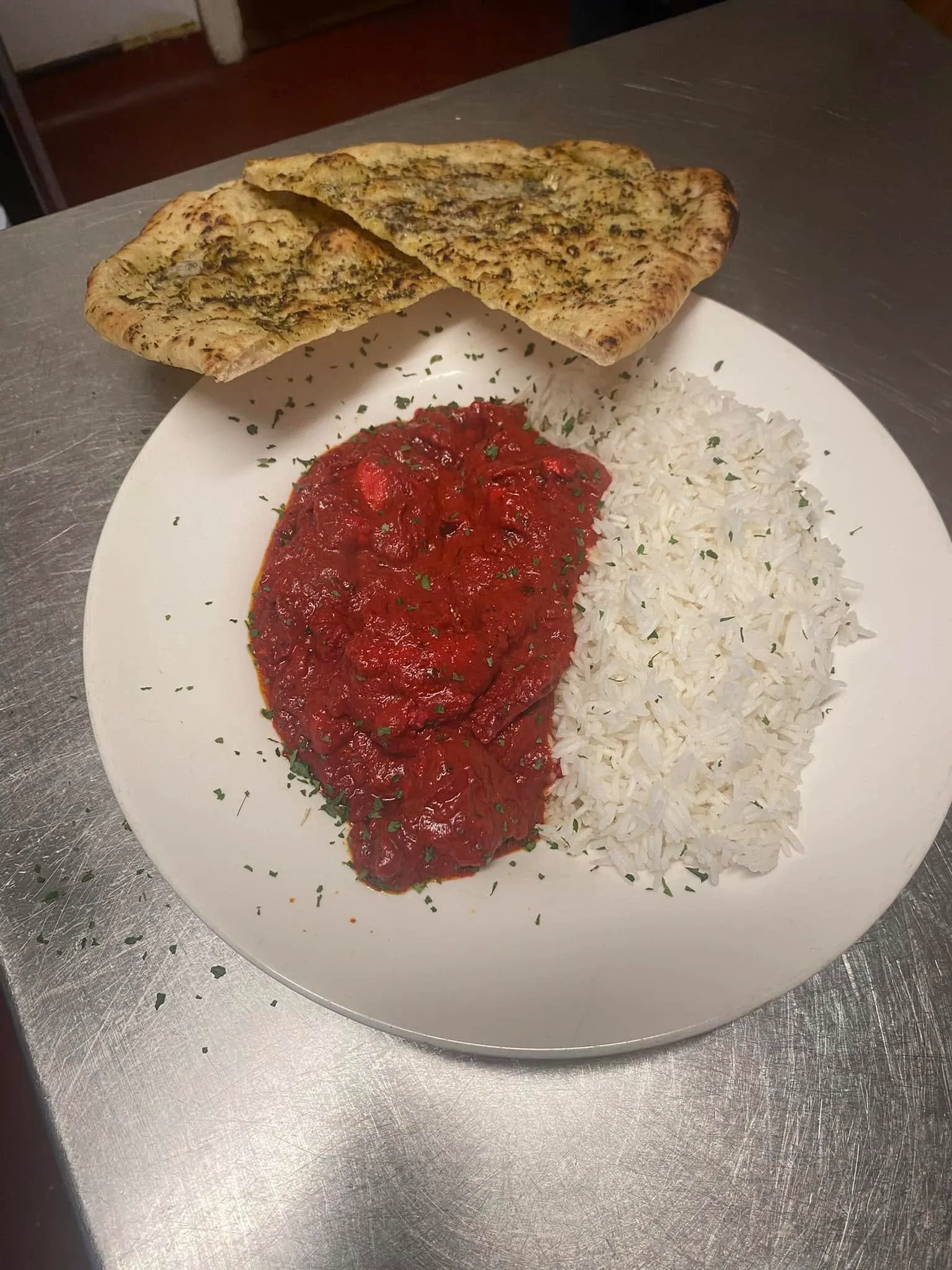 A white plate topped with curry, rice and a naan bread.
