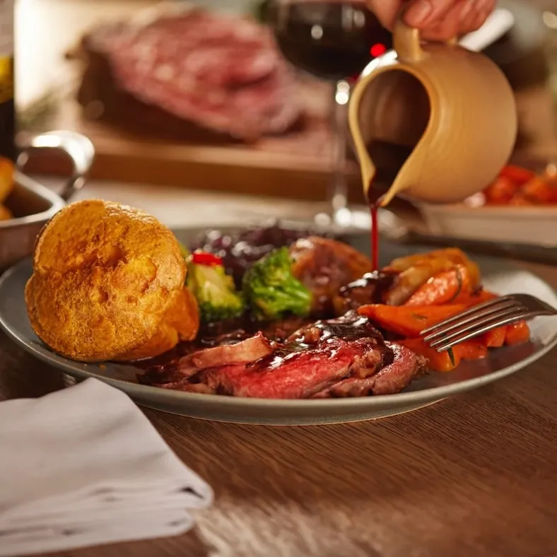 A person pouring gravy on a roast dinner.