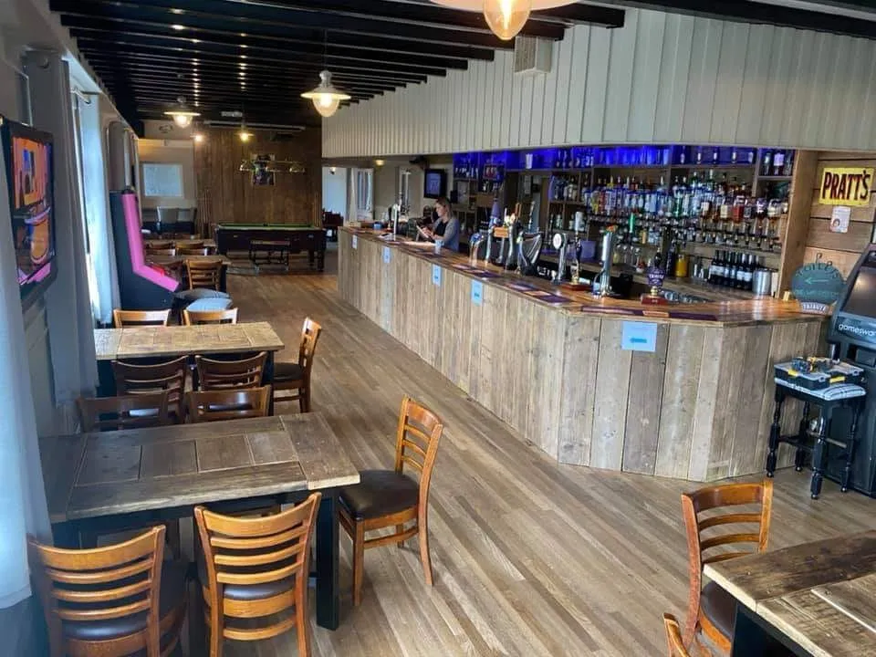 A restaurant with wooden tables and chairs and a bar.