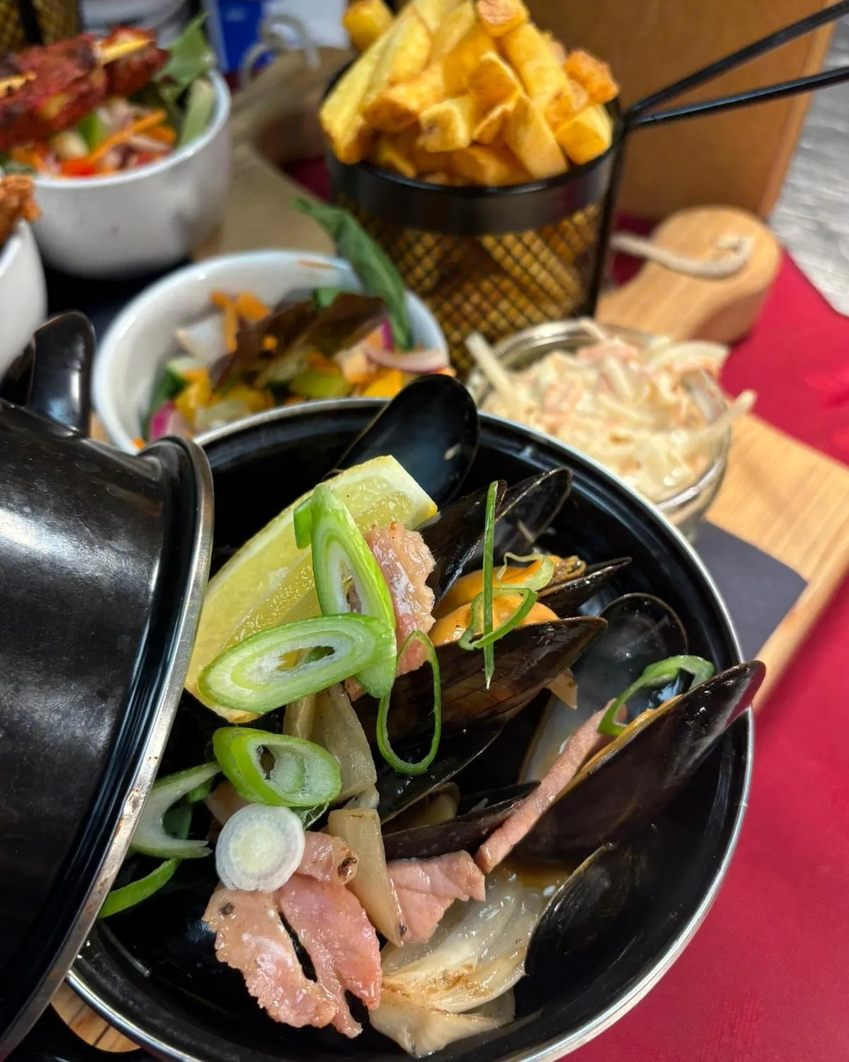 A bowl of mussels on a table with side dishes.